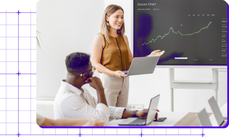 Woman presents financial data in office, engaging colleague with stock chart on monitor.