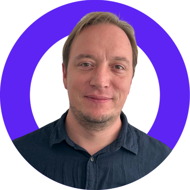 Smiling middle-aged man in blue shirt against purple backdrop, conveying professionalism and warmth.