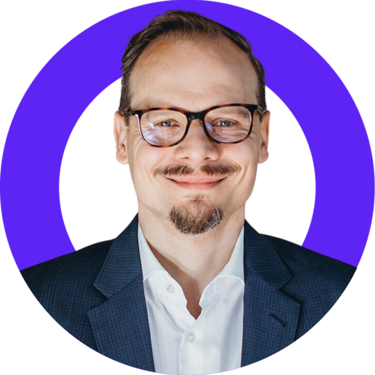 Professional man in glasses smiles in blue blazer, framed against a purple background.
