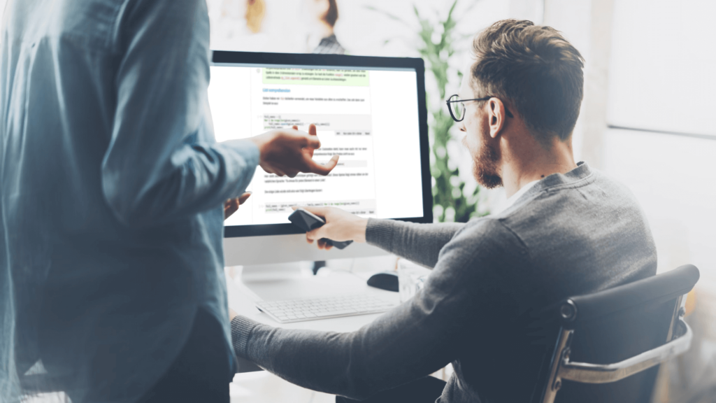 Two professionals analyze data on a computer in a modern, collaborative office setting.