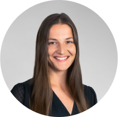 Confident woman in professional attire smiles in a polished headshot against a gray background.