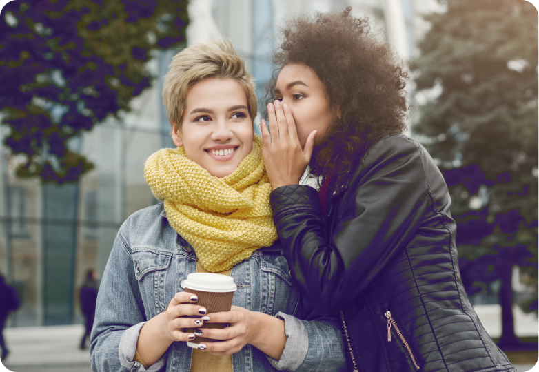 Zwei junge Frauen teilen ein Geheimnis in urbaner Herbstkulisse.